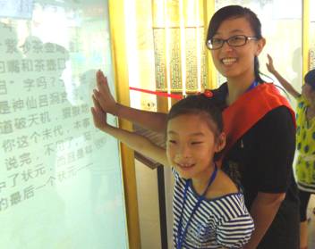 苏州市名人馆的大学生志愿者在清代厅指导小观众使用触摸屏参与互动项目。